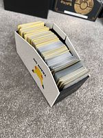 White Pokémon Elite Trainer Box with Pikachu graphic on the side, filled with many Pokémon cards of various edges and thickness.