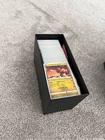 Black Elite Trainer Box filled with numerous Pokémon trading cards visible from the top, with a Japanese Magmar card on top.
