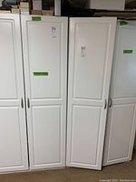 Front view of two tall white particle board cabinets side by side