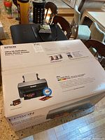 Sealed Epson R260 printer box on countertop alongside HP printer and accessories.