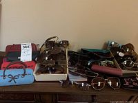 Eyeglasses and sunglasses displayed on a wooden surface along with several different eyeglass cases.