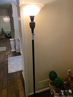 Full view of floor lamp standing against a wall, turned on with light shining through glass shade.
