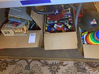 Boxes containing board games Monopoly and Boggle alongside other vintage toys, including more building kits and playset parts.