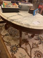 Side view showing the white marble table top with grey veins and the dark carved wooden base with curved legs.