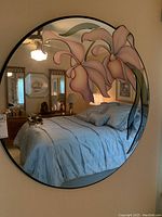 Round wall mirror mounted on wall with pastel floral applique, reflecting bedroom interior.