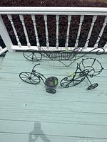 Photo showing all three metal plant stands arranged on deck floor including the wheelbarrow cart and two tricycle stands