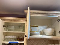 Open cabinet shelves showing multiple clear rectangular glass Pyrex baking dishes stacked together, along with glass serving platters, and white ceramic Pyrex dishes stacked.