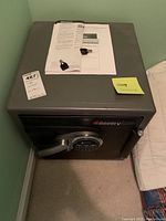 Front and top view of black Sentry Safe with digital keypad lock, owner's manual and keys on top.