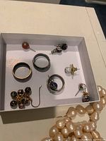 Box with multiple jewelry pieces including cloisonné bead earrings, three rings, and faux pearl necklace strand.