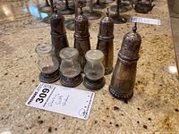 Four sterling silver salt and pepper shakers on granite countertop with auction lot and tag visible