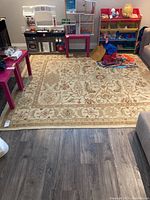 Large area carpet shown laid out on wood flooring with some children's toys and furniture around it, showing overall design and size.