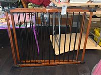 Full view of wooden and metal child safety gate folded and resting on a table against furniture and household items