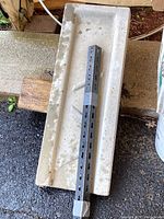 Full top view of rectangular concrete drainage pad placed on a concrete surface with a metal post taped on it to show scale.