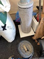 Full view of the PROfilter pump covered in gray felt beside a coiled garden hose on the floor with additional gardening items around.