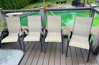 Four matching patio chairs lined up on outdoor deck near pool with green pool cover visible in background. Chairs have metal frames and beige woven fabric seating.