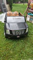 Front view of black battery-operated ride-in Cadillac toy car with 'Cadillac' script on windshield and tan seats.