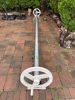 Full view of the pool cover roller lying on a patio, showing metal roller tube and white crank handle on one end.