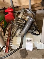 Photo showing electric hedge clippers with red blade guard and Skilsaw circular saw cords coiled together on a white surface beside a wood backdrop.
