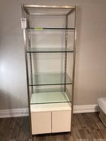 Front view of the tall shelving unit showing 4 glass shelves and white cabinet base.