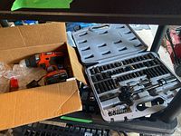 Photo showing Black & Decker cordless drill in cardboard box beside open plastic case with Stanley socket set.