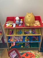 Wooden storage rack with nine removable colored plastic bins filled with toys and small items.