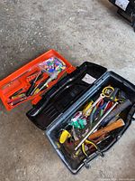 View of open black plastic tool box with several hand tools inside including hammer, pliers, screwdrivers, tape measures.