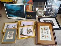 Multiple framed and unframed artworks on floor including dolphin print, coat of arms, tropical floral prints, black and white animal figure drawing, and other framed paintings