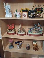 Wide view of the bird and floral figurines arranged on shelves showing a variety of bird species, floral decorations, and bases