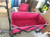 Red foldable wagon with black metal frame and wheels, fabric seating area, foldable design shown assembled