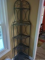 Full view of the metal corner shelving unit placed in a corner near a window, showing its height and decorative metalwork.