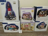 Front view of all six boxed Department 56 village buildings arranged in two rows showing box art and titles.