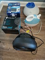 Photo of all four items on floor: Arctic Air personal fan box, Avalon Max Cool fan box, blue and white humidifier/vaporizer, black fan.