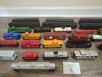 Photo showing 30 HO scale train cars arranged on a floor including black passenger cars, colored cabooses, and tankers.