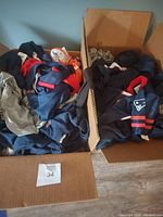 Two full boxes of assorted new with tags sports apparel visible including navy items with New England Patriots logos.