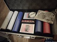 Open metal case showing WSOP poker chips in white, blue, and red, two decks of cards, and dealer button.