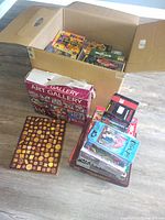 Box filled with assorted used jigsaw puzzle boxes including Gallery brand and others showing various puzzle themes.
