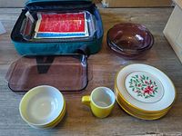 Photo of full lot contents arranged on the floor including plates, bowls, mug, and glass baking dishes in carrying bag