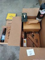 Box containing shoe shine kits, shoe shine supplies, a vintage bottle, wooden cigar boxes, and brushes.