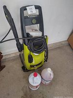 Front view of Sun Joe SPX3000 pressure washer with attached wand and coiled power cord, plus two cleaning solution bottles on the floor.
