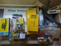 Overview of the lot showing boxed Village Streetcar set, yellow accessory boxes, and clear bin with assorted items