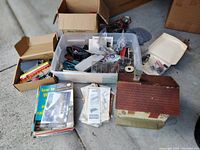Wide view of the lot showing magazines, boxes with model train parts, and a building model with a brown roof.