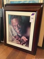 Framed photograph showing Bill Russell smiling, wearing a checked blazer, holding multiple trophy rings in his hands.