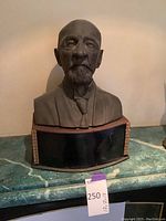 Front view of bronze bust of a man with detailed facial features and suit on a decorative black base.