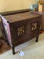 Front and side views of Asian style cabinet with decorative gold-tone panels and hinged doors.