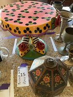 Image showing colorful, hand painted wooden cake stand with decorative feet and plants in the background.