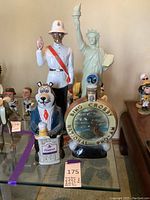 Full view of all three ceramic liquor decanters on glass shelf showing a Royal Canadian Mounted Police figure, a cartoon bear holding a beer mug, and a bing Crosby golf commemorative decanter.