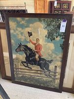 Full view of framed lithographic print showing the huntsman on horseback jumping a fence with lot tag visible