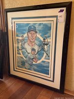 Full view of framed Mickey Mantle lithograph leaning against a wall on a wood floor. Shows the complete framed artwork with the New York Yankees baseball player image.