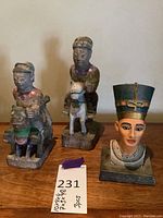 Frontal view of all three items together showing the Queen Nefertiti bust to the right and two Asian wooden figures on the left and center.