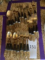 Cocktail forks and spoons arranged on a table showing embossed decorative gold tone handles with Siamese face motifs.